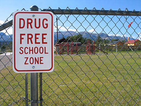 Drug Free School Zone sign with playground behind a fence.