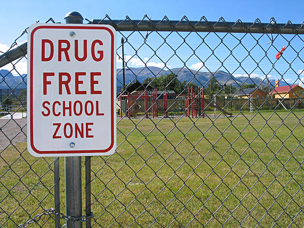 Drug Free School Zone sign with playground behind a fence.